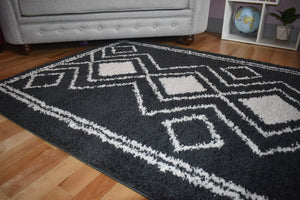 Black and white geometric patterned rug on a wooden floor with a gray sofa in the background.