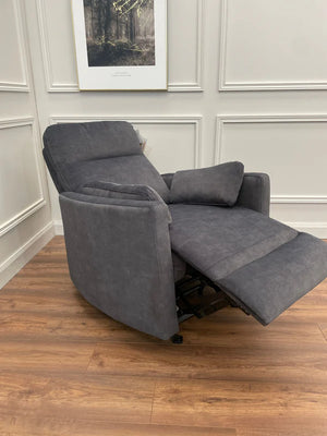 A gray velvet fabric rocking recliner positioned in a room with wooden flooring and a photograph on the wall.