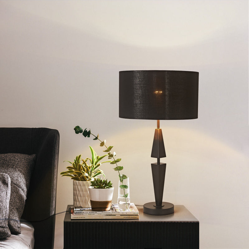 Black table lamp on a side table with a plant and books in a room setting.