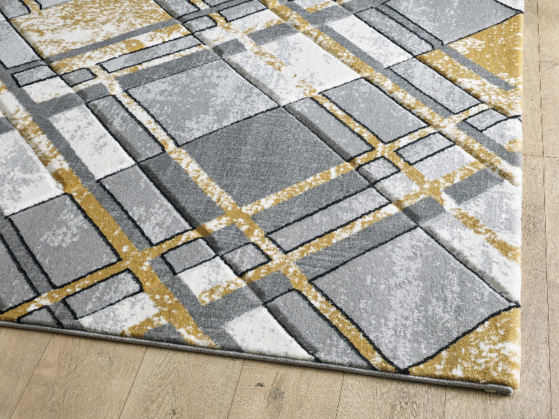 Geometric patterned rug with squares in gray, white, and gold on a wooden floor.
