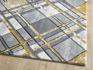 Geometric patterned rug with squares in gray, white, and gold on a wooden floor.