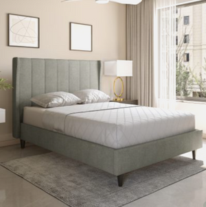 Gray upholstered bed in a modern bedroom with large windows.