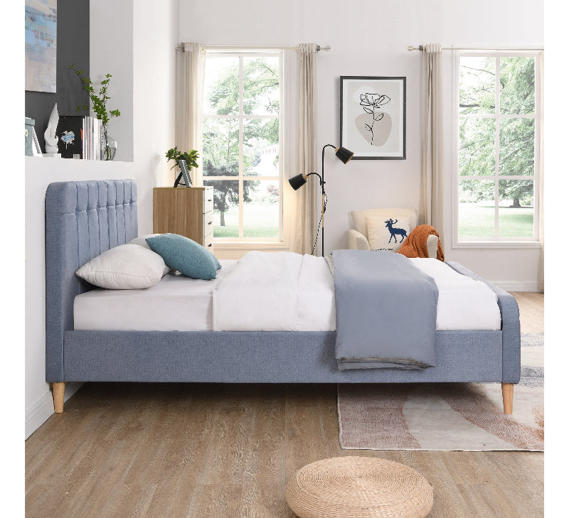 Blue upholstered bed in a bright bedroom with large windows.