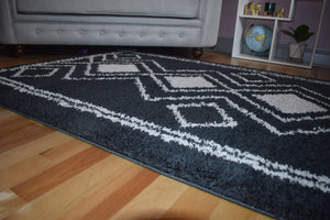 Gray area rug with white geometric pattern on a wooden floor, with a gray sofa and decorative items in the background.