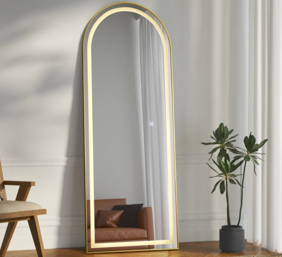Full-length mirror with gold frame in a room with a chair and plant.