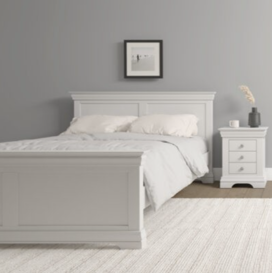 Ivory bed in a bedroom with a nightstand and framed picture on the wall.