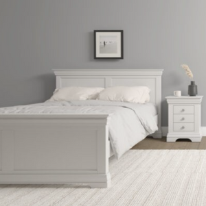 Ivory bed in a bedroom with a nightstand and framed picture on the wall.