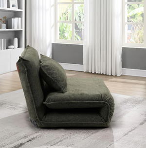 Green floor pillow in a room with large windows and a bookshelf.