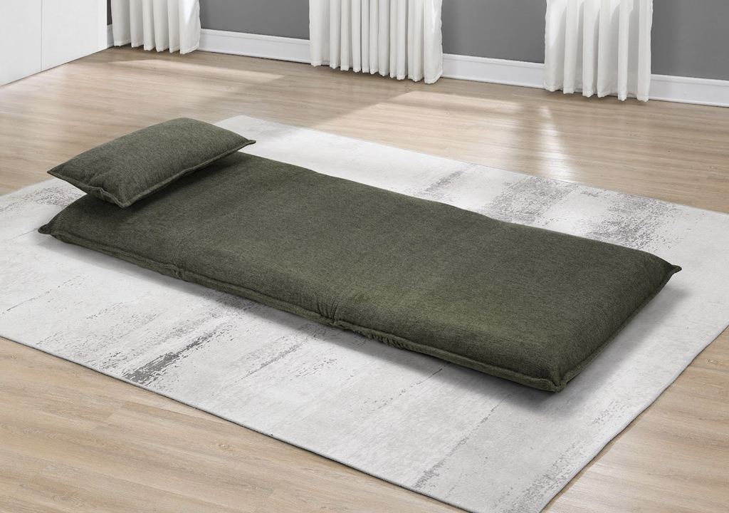 Green futon mattress on a rug in a room with wooden flooring and white curtains.