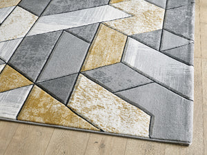 Geometric patterned rug with shades of gray, beige, and white on a wooden floor.