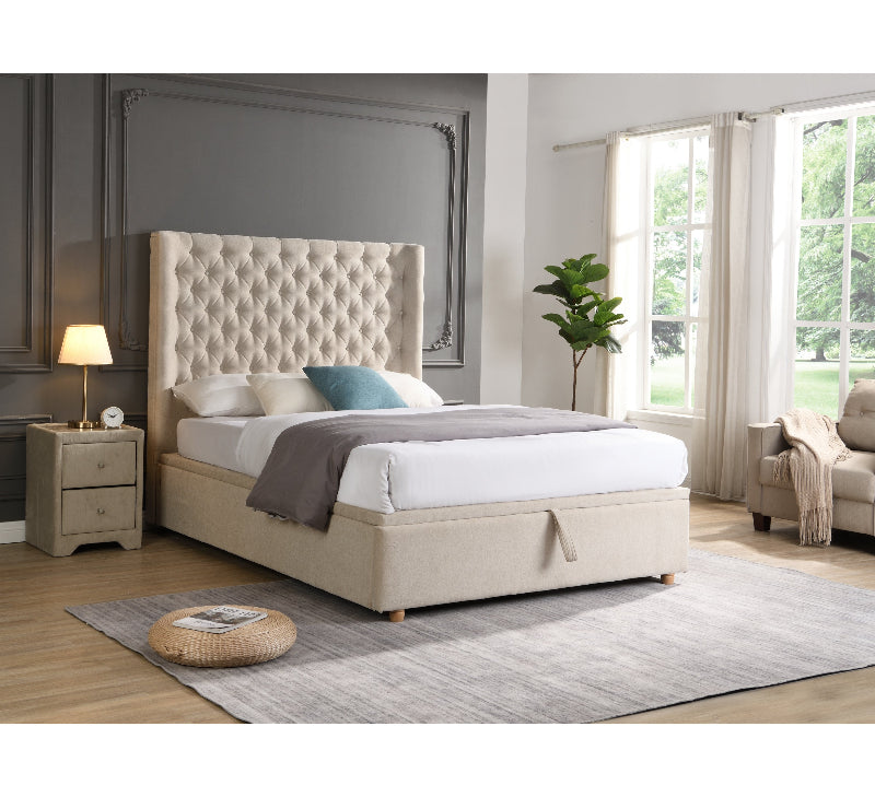Beige upholstered bed in a bedroom setting with a lamp and plant.