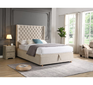 Beige upholstered bed in a bedroom setting with a lamp and plant.