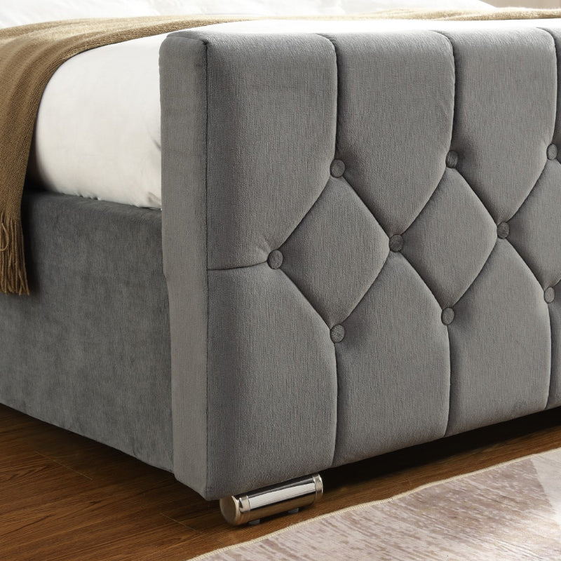 Grey tufted headboard on a bed with a wooden floor and beige blanket.