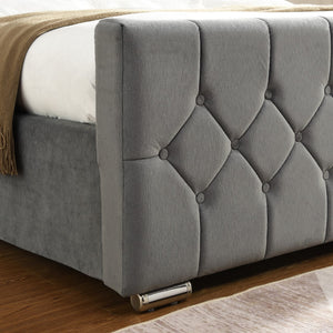 Grey tufted headboard on a bed with a wooden floor and beige blanket.