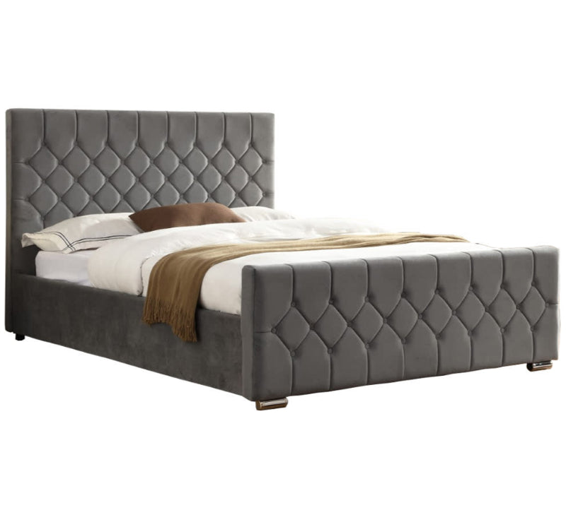 Grey tufted bed with white bedding and a brown blanket on a white background