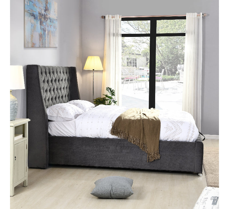Gray upholstered bed in a bedroom with a large window and decor elements.