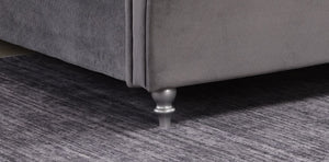 Close-up of a grey upholstered chair with metallic legs on a textured grey floor.