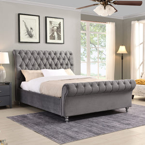 Grey upholstered bed in a bedroom with large windows and decorative elements.