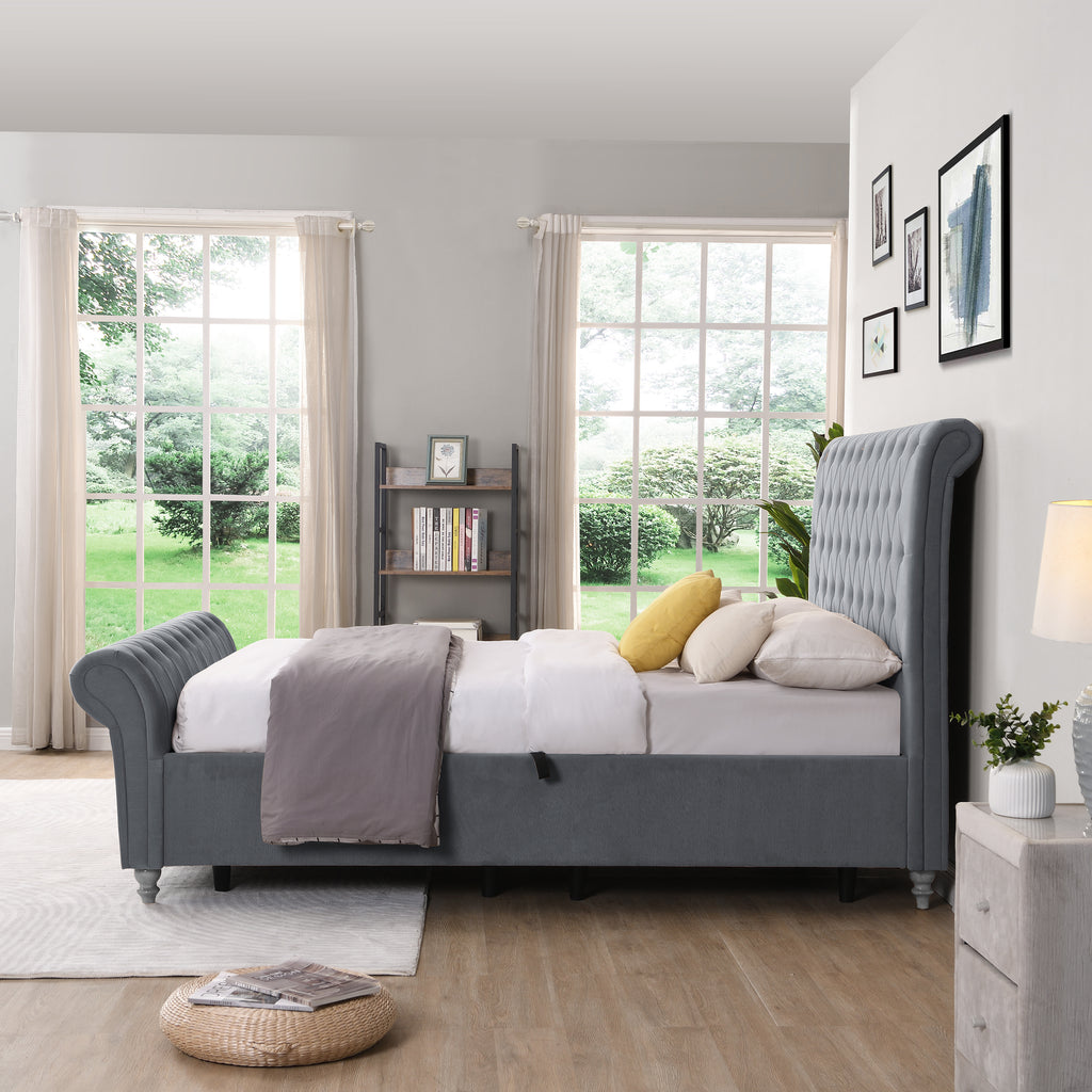 Gray upholstered bed in a bright bedroom with large windows and a lamp.