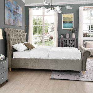 Neatly made bed in a bedroom with mink upholstered headboard, white bedding, and decorative pillows.
