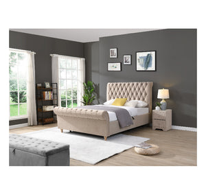 Beige upholstered bed in a bedroom with grey walls and white curtains.