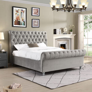 Grey upholstered bed in a bedroom with a fireplace and framed pictures on the wall.