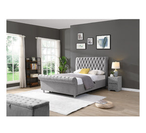 Grey upholstered bed in a modern bedroom with grey walls and large windows.