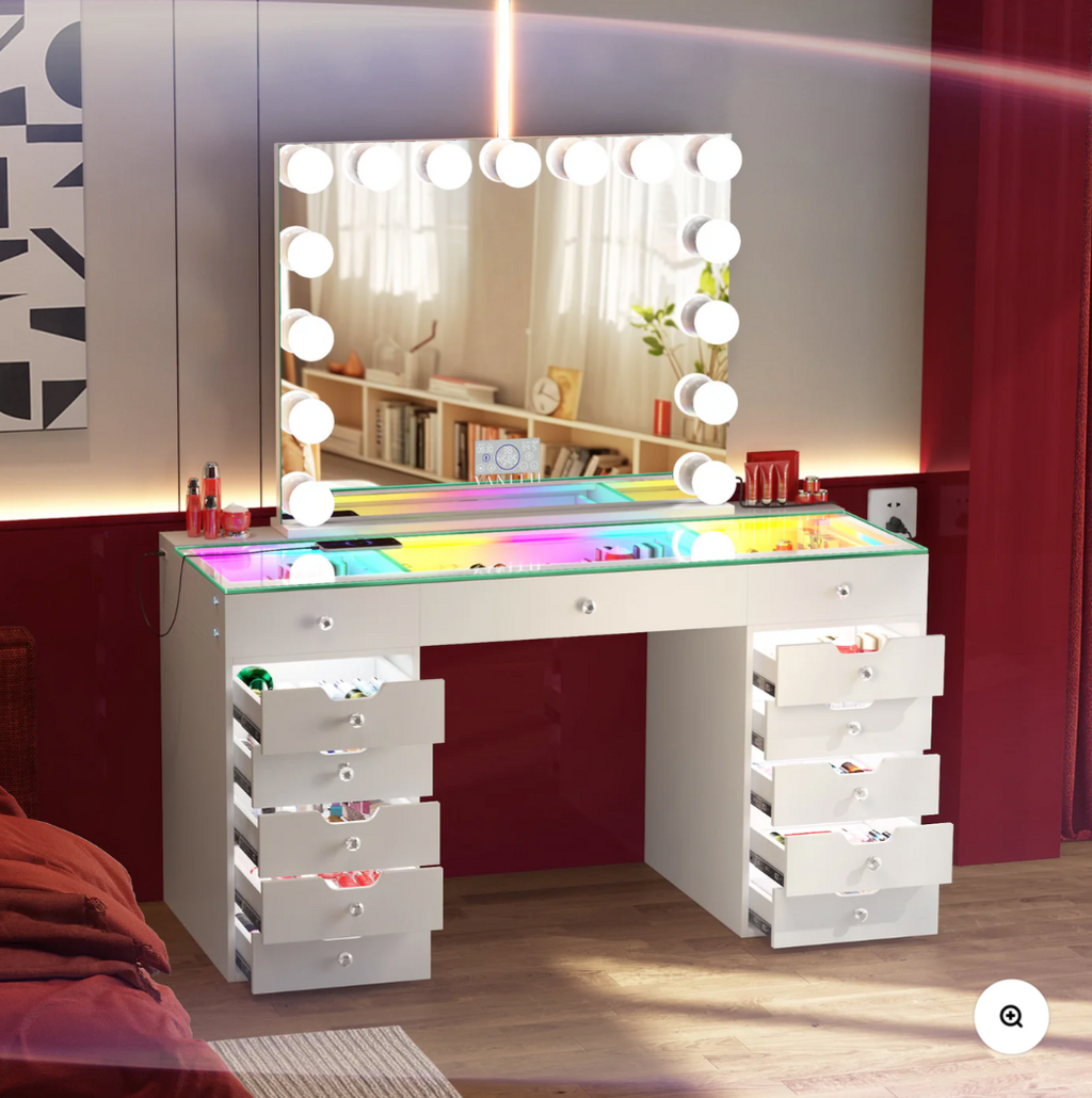 White vanity desk with multiple drawers and a large mirror with lights in a room.