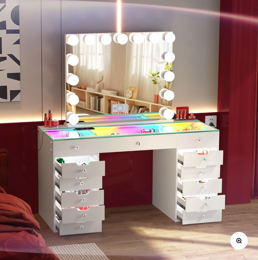 White vanity desk with multiple drawers and a large mirror with lights in a room.