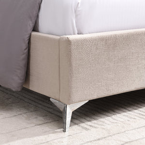 Close-up of a beige upholstered bed frame with a white mattress and gray bedding.