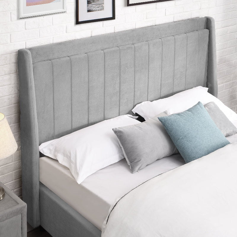 Grey upholstered bed with white bedding and blue pillows against a white brick wall.