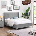 Grey upholstered bed in a well-decorated bedroom with white walls, framed art, and a plant.