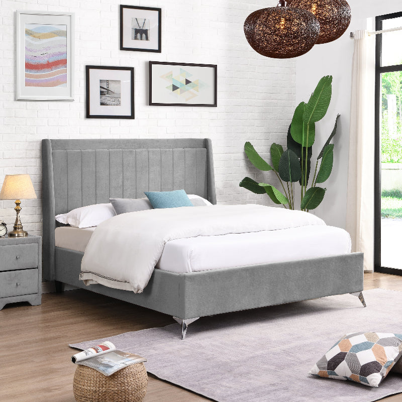 Grey upholstered bed in a well-decorated bedroom with white walls, framed art, and a plant.