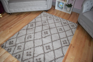 Grey patterned rug on a wooden floor with a gray sofa and white bookshelf in the background.