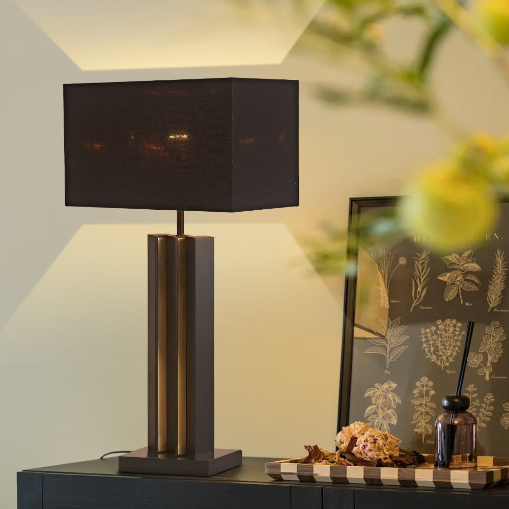 Table lamp with a black shade on a dresser next to a decorative plant and framed artwork.