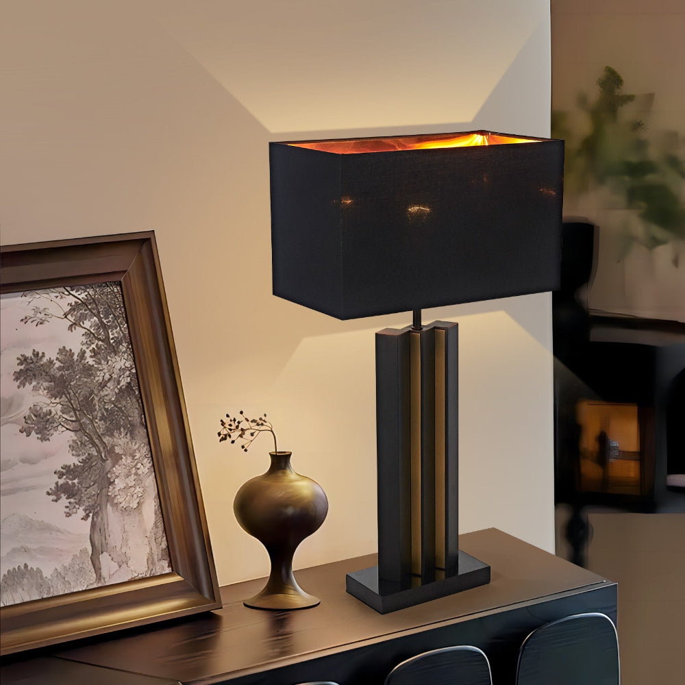 Modern table lamp with black shade on a wooden surface, next to a framed picture and decorative vase.
