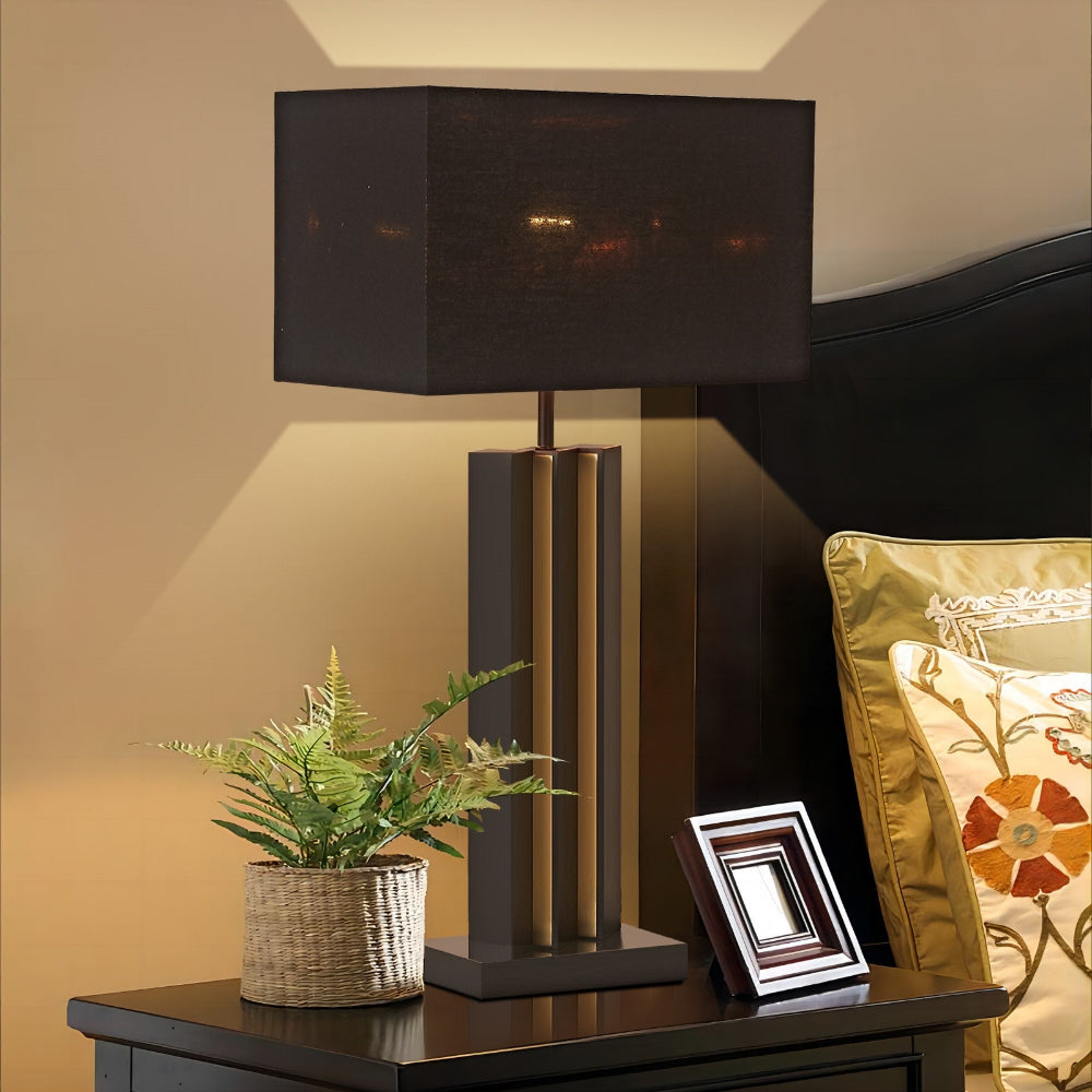 Black table lamp on a wooden surface with a plant and decorative pillow in the background
