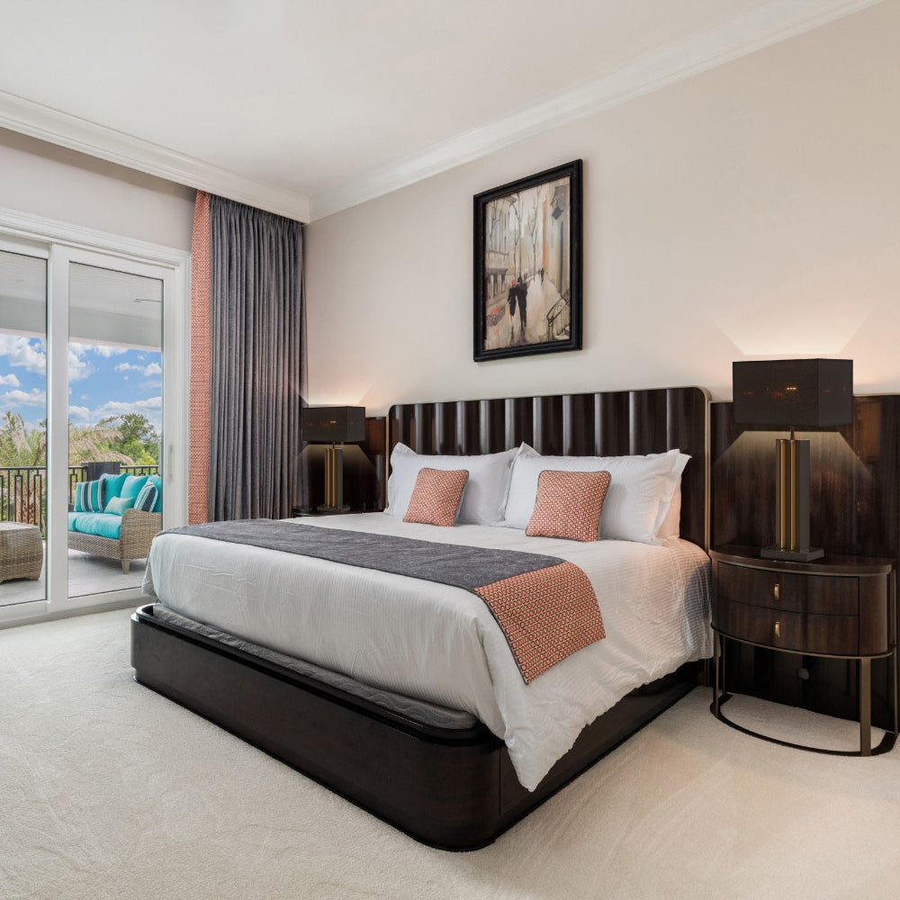 Modern bedroom with a large bed, nightstands, and a view of the outdoors through a sliding glass door.