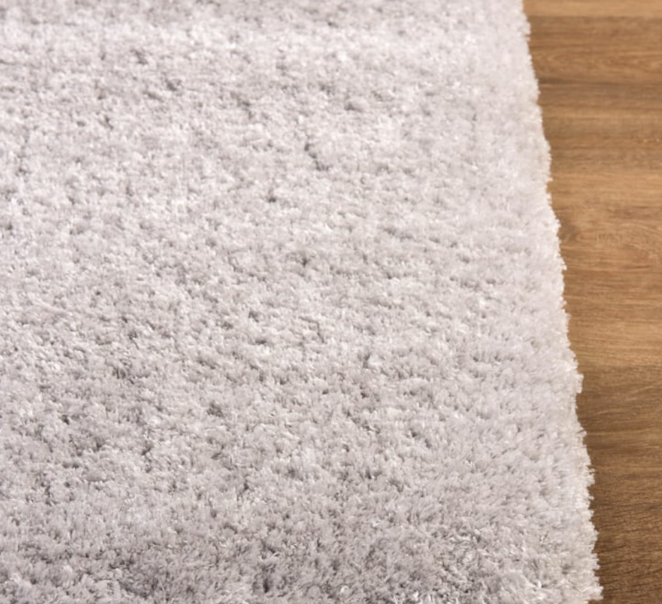 Close-up of a textured gray carpet corner meeting a wooden floor.