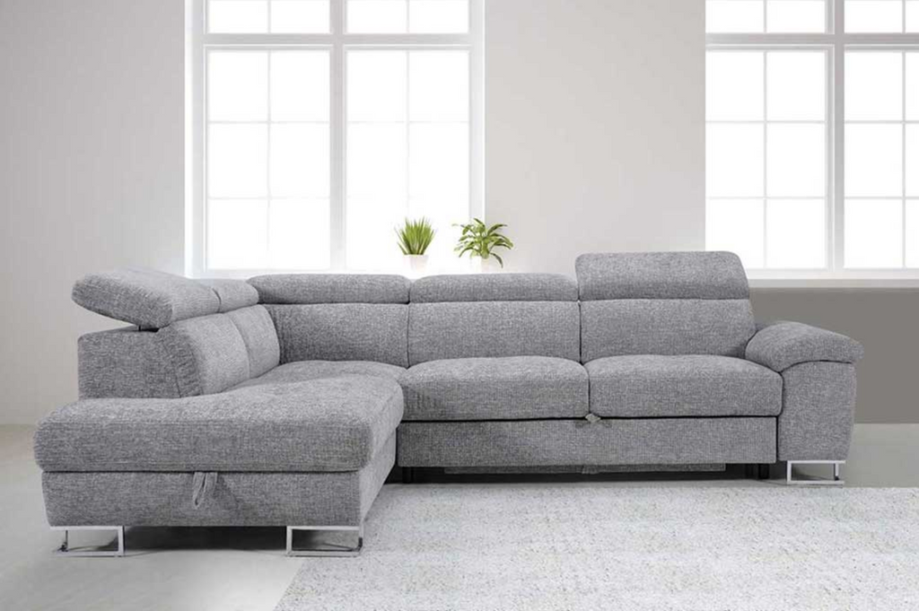 Gray sectional sofa in a room with large windows and plants.