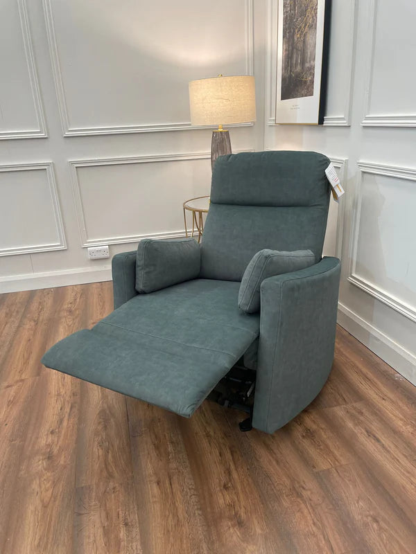 A green velvet fabric rocking recliner positioned in a room with wooden flooring and a photograph on the wall.
