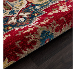 Close-up of a patterned rug with red, blue, and beige colors on a dark floor.