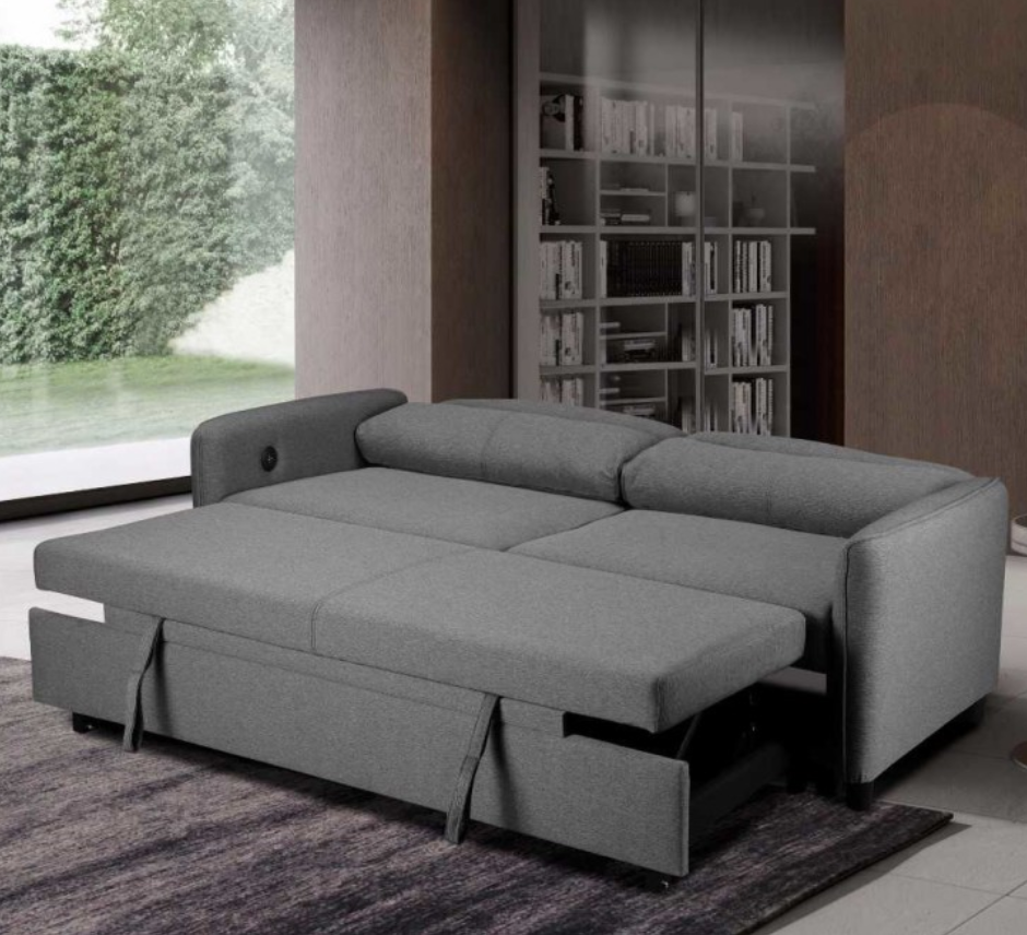 Gray sectional sofa with pull-out bed in a room with bookshelf and window.