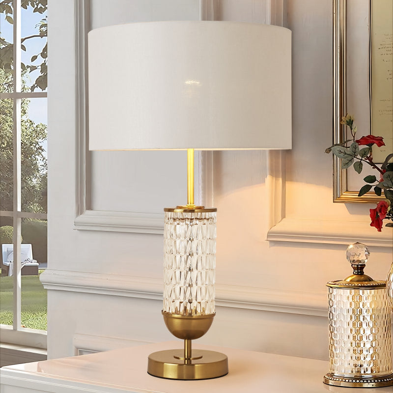 Decorative table lamp with a gold base and white shade on a surface near a window.