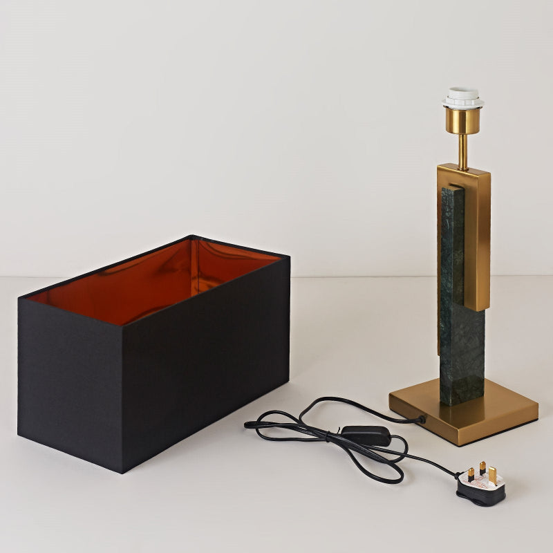 Modern lamp with black rectangular shade and gold base on a white surface.