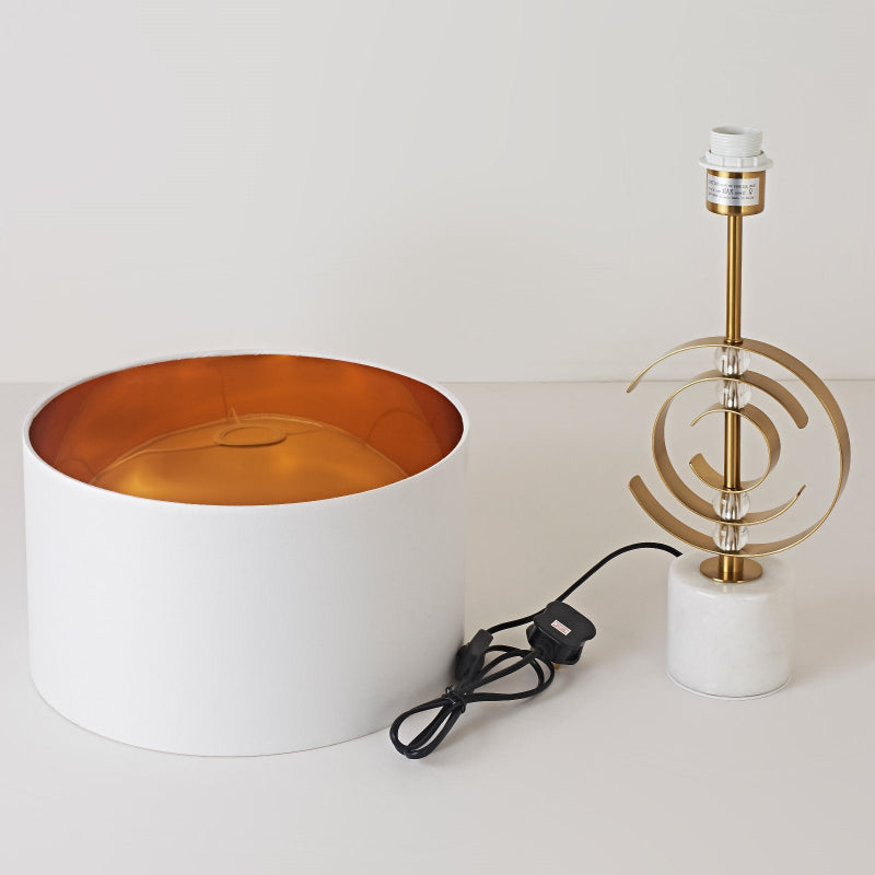 Modern lamp with white base, gold interior, and decorative metal shade on a light background