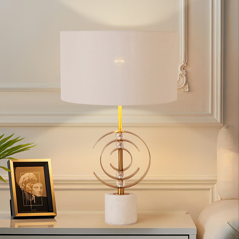 Decorative table lamp with a white shade and gold accents on a shelf.