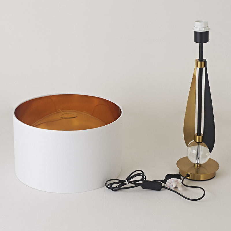 Modern table lamp with white base and gold interior, next to a white cylindrical container on a light gray background.