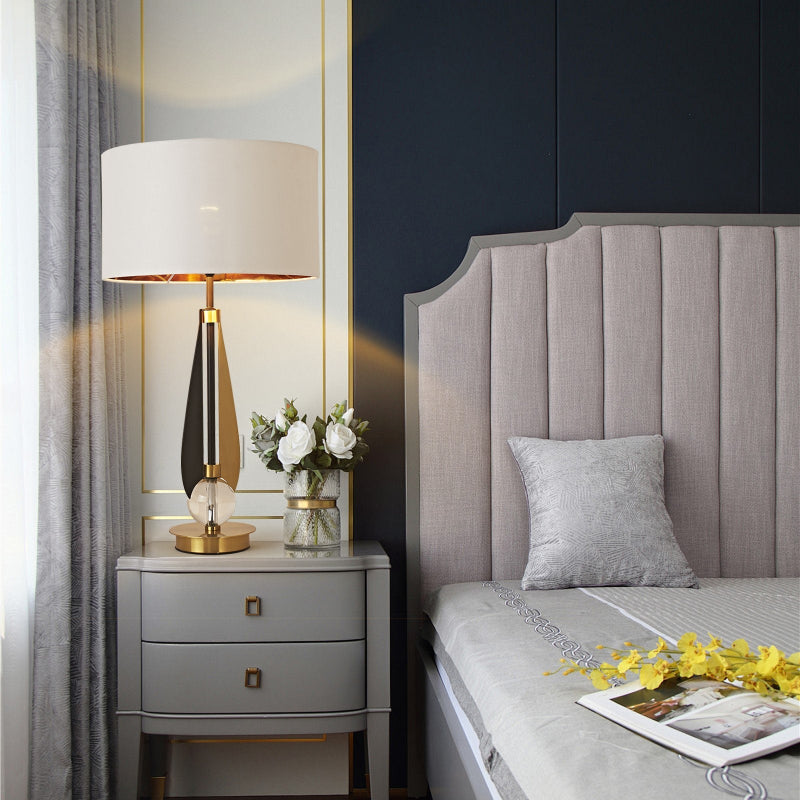 Modern bedroom with gray upholstered headboard, nightstand with lamp, and decorative elements.