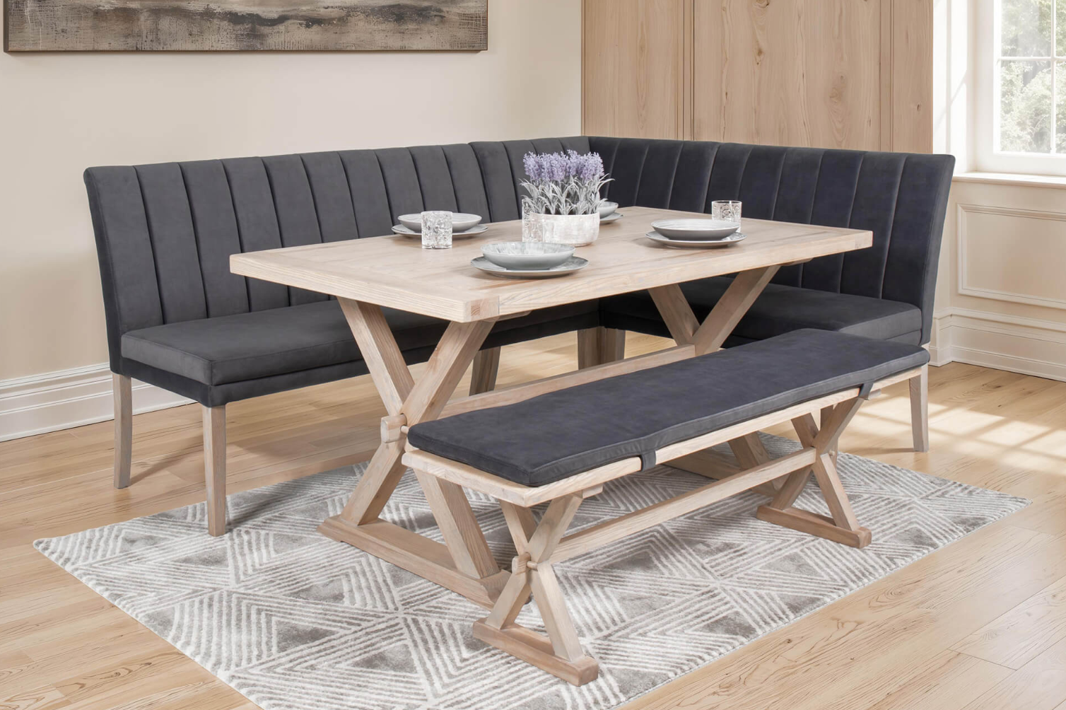 Dining room setup with a wooden table and grey upholstered benches on a patterned rug.
